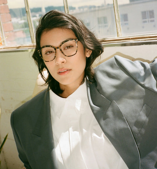 Person in glasses and suit jacket sitting by a window.