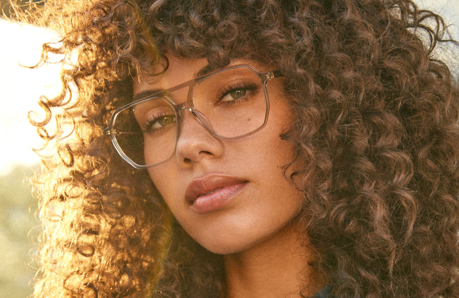 Person with curly hair and glasses in soft sunlight.